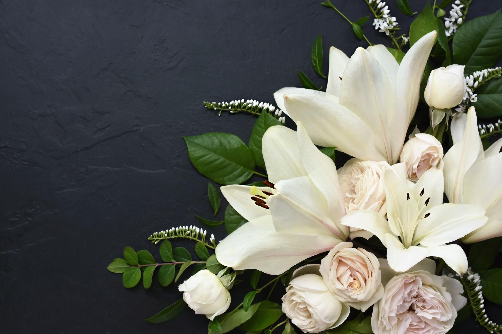 Weiße Lilien und Rosen, zu einem Strauß vor dunklem Hintergrund arrangiert.