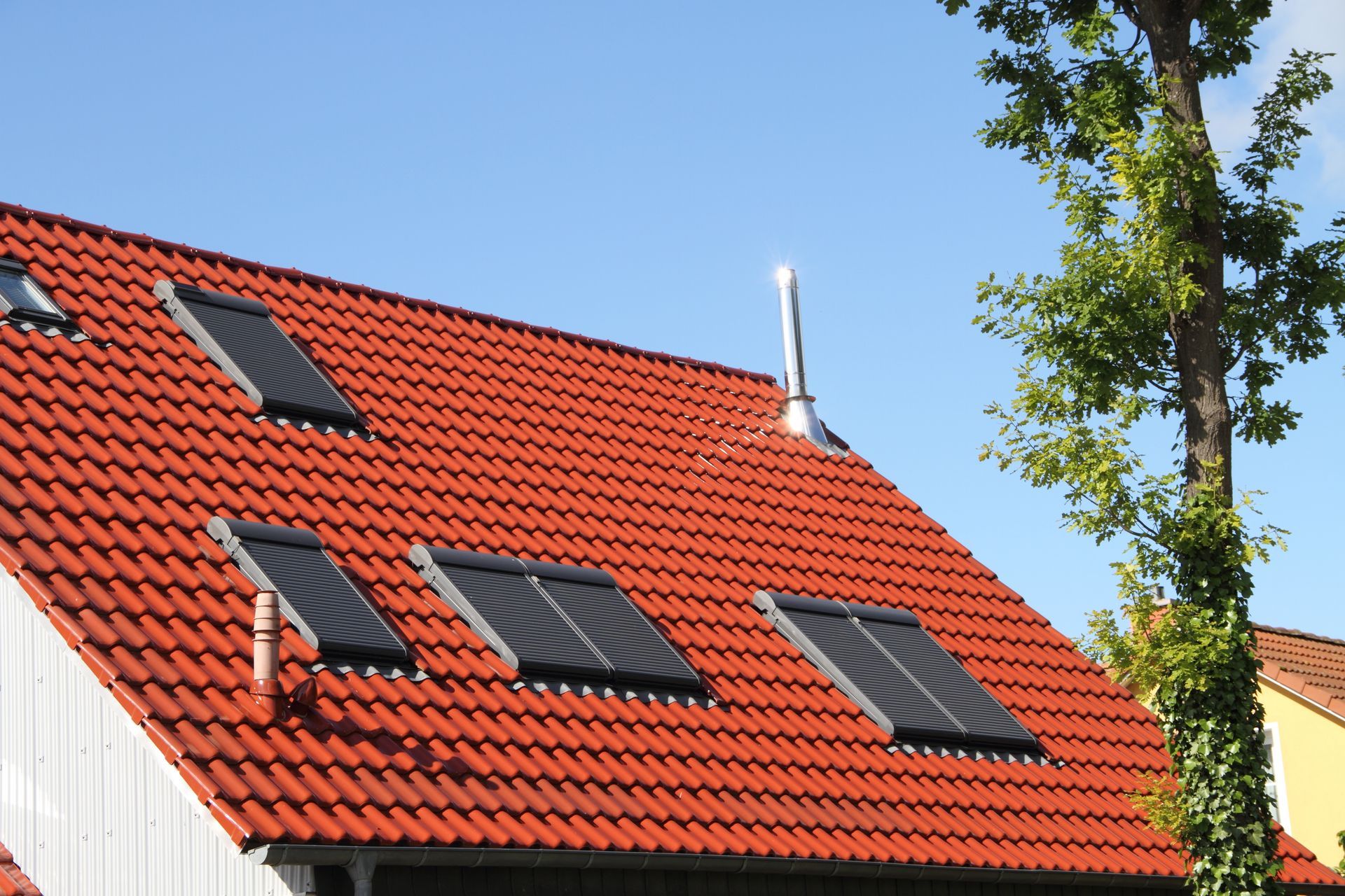 Toit de tuiles rouges avec panneaux solaires et cheminée.