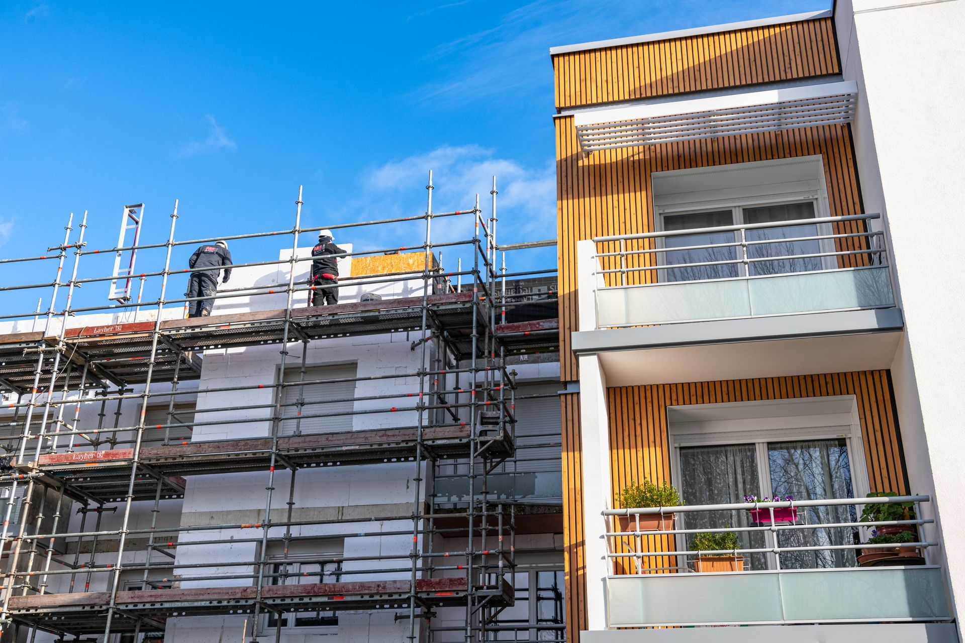 Des ouvriers du bâtiment travaillent sur des échafaudages, à l'extérieur d'un immeuble avec balcons.