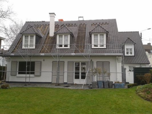Maison au toit gris en cours de réparation ; échafaudage devant, pelouse au premier plan.