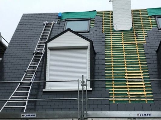 Toiture en ardoise en cours d'installation, échelle, échafaudage et lucarne avec volet.