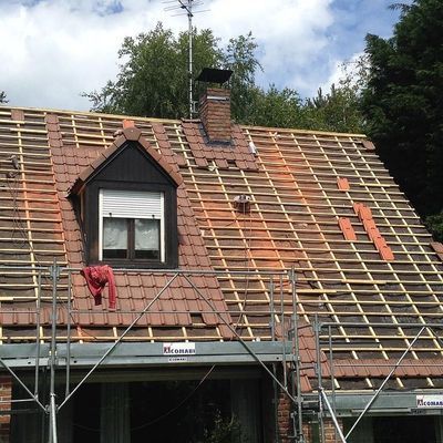 Toiture en construction : tuiles rouges, chevrons apparents, lucarne, échafaudages.