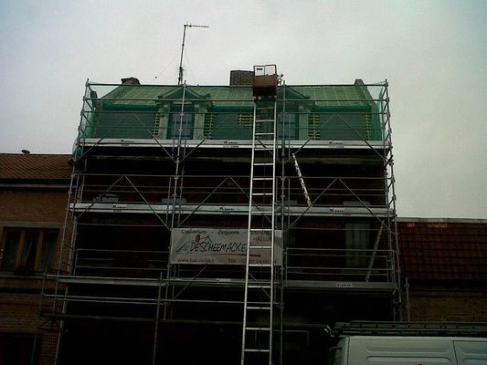 Bâtiment en rénovation avec échafaudages, filets verts et échelle.