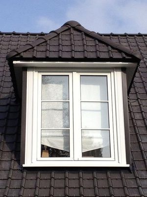 Lucarne à cadre blanc, sur un toit de tuiles sombres, sous un ciel bleu.