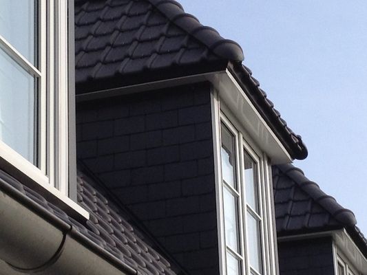 Toit et bardage sombres avec encadrements de fenêtres et moulures blancs.