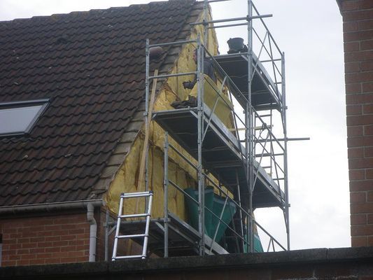 Échafaudage sur le côté de la maison pendant des travaux d'isolation, avec des matériaux jaunes visibles.
