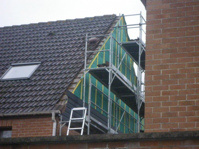 Échafaudage à côté du toit d'une maison en construction ; une bâche verte recouvre la zone non finie.