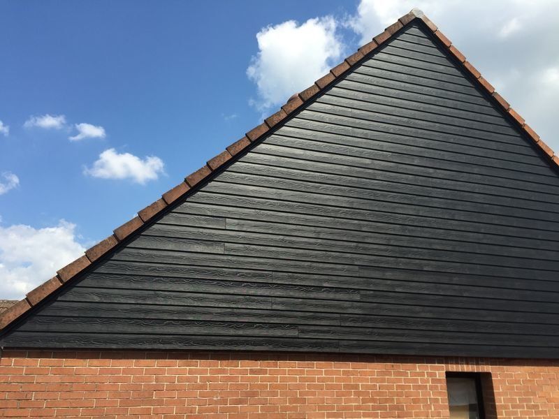 Bardage en bois noir sur une section de toit triangulaire, au-dessus d'un mur de briques.