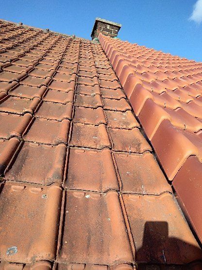 Toit de tuiles en terre cuite avec une cheminée sur fond de ciel bleu, certaines tuiles sont décolorées.