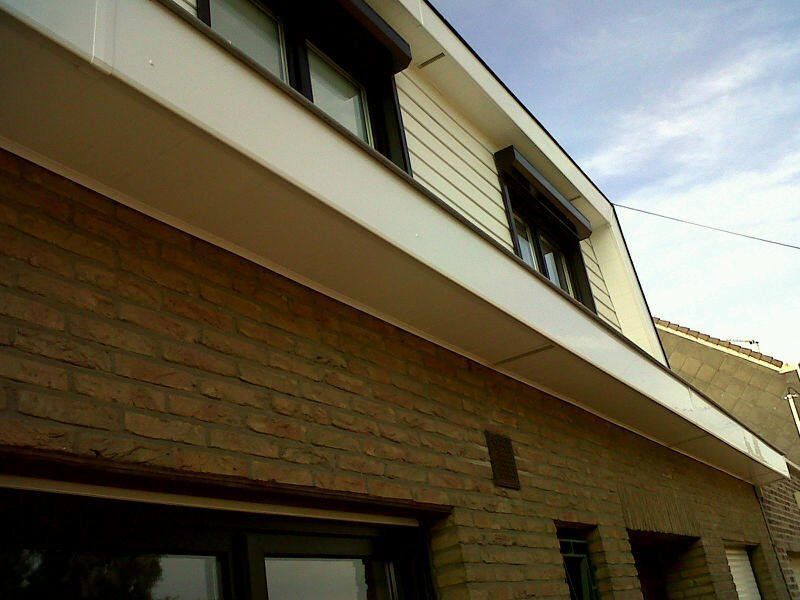 Bâtiment en briques avec encadrements blancs, bardage beige et volets foncés. 