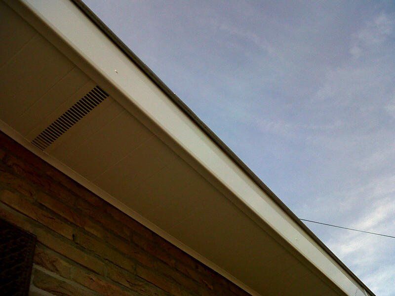 Gros plan sur un avant-toit de maison. Boiseries blanches, parement en briques brunes.