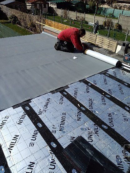 Personne posant des matériaux de couverture sur un toit plat. Matériaux gris, poutres noires, cadre extérieur ensoleillé.