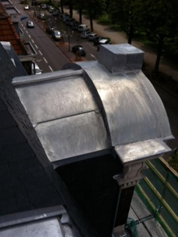 Gros plan sur un détail architectural recouvert de plomb sur le toit d'un bâtiment, donnant sur une rue avec des voitures garées.