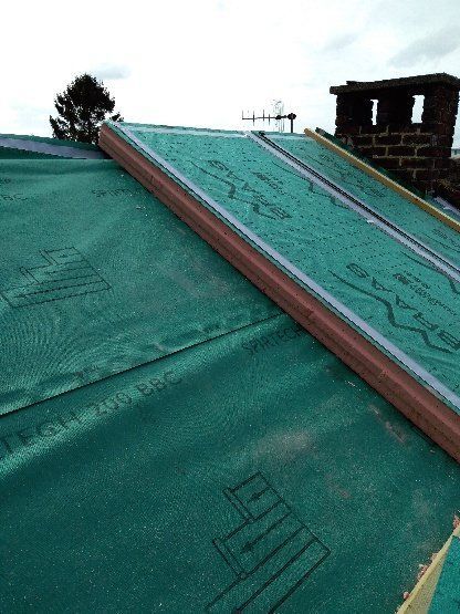 Installation d'un matériau de toiture végétalisée sur un toit, avec une cheminée en arrière-plan.