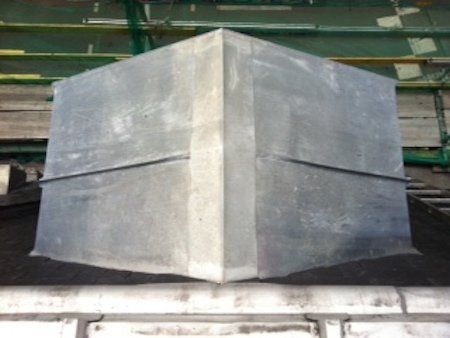 Un grand cube de métal gris, probablement recouvert de plomb, repose sur une surface sombre, les soudures étant visibles aux angles.