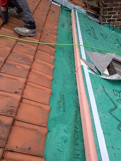 Gros plan sur la pose de tuiles, avec la sous-couche verte et les jambes d'un ouvrier visibles.