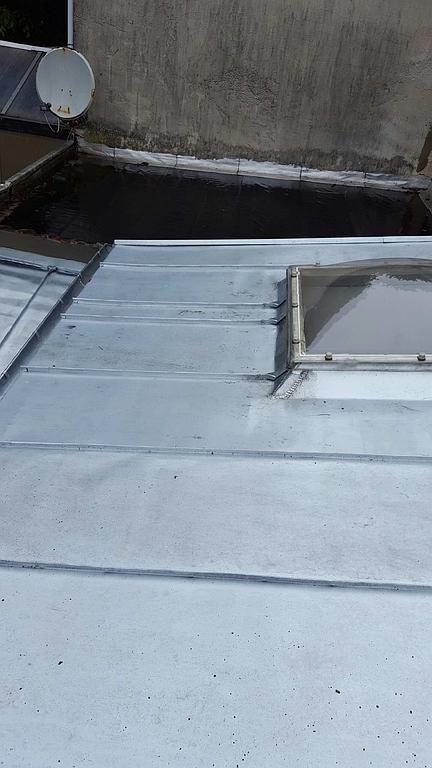 Toiture métallique avec un petit puits de lumière et une antenne parabolique.