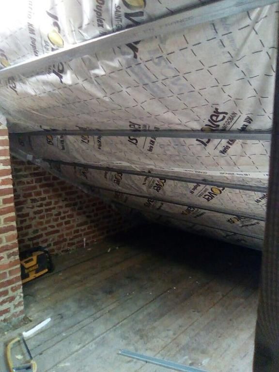 Intérieur d'un grenier isolé avec poutres apparentes. Mur en briques à gauche, plancher en bois.