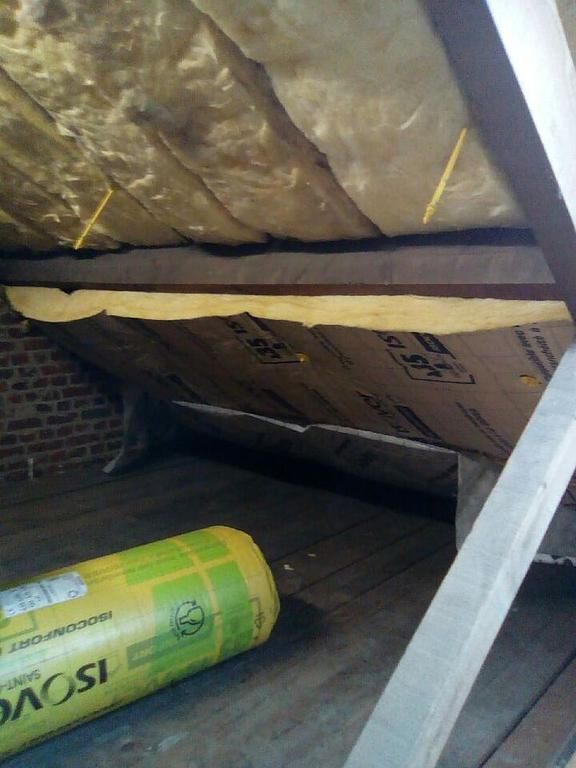 Intérieur du grenier avec isolation installée entre les chevrons. On aperçoit un rouleau d'isolant jaune et des poutres en bois apparentes.