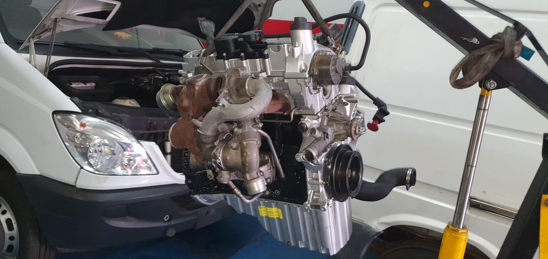 El motor de una furgoneta blanca está siendo reparado en un taller.