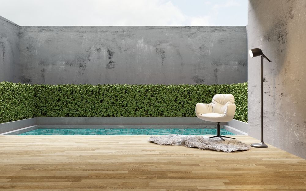 Patio moderno con una piscina estrecha, seto verde, pared gris y tumbona color crema sobre una alfombra.