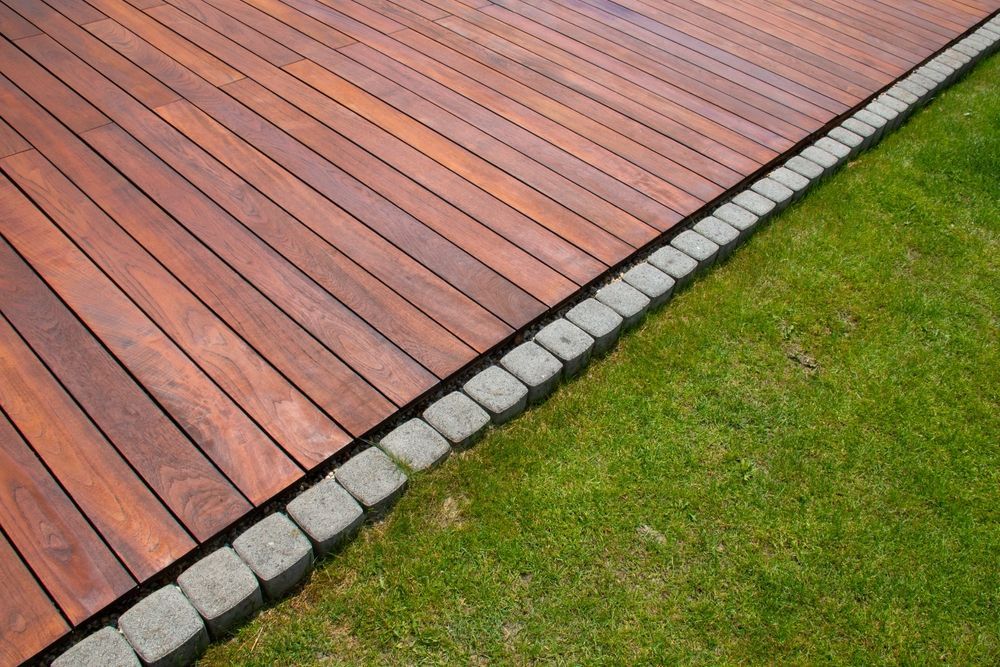 Terraza de madera bordeando un muro de piedra junto a césped verde.
