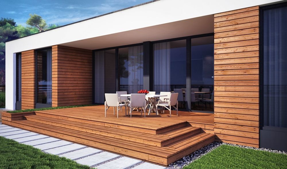 Patio de casa moderna con terraza de madera, mesa de comedor al aire libre y grandes puertas corredizas de vidrio.