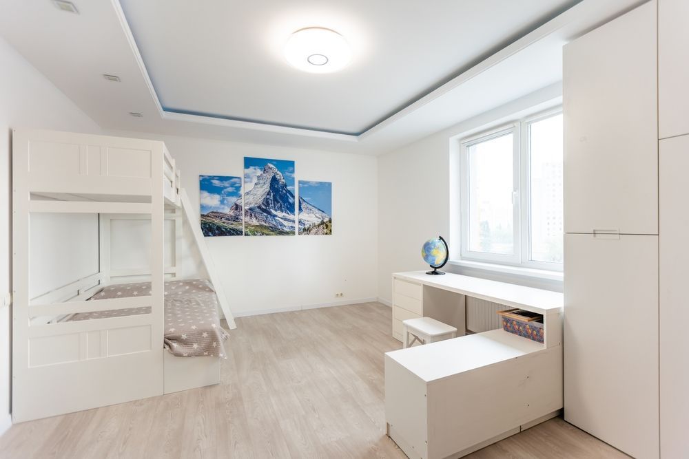 Habitación blanca luminosa con litera, escritorio junto a la ventana y cuadro de montaña en la pared.