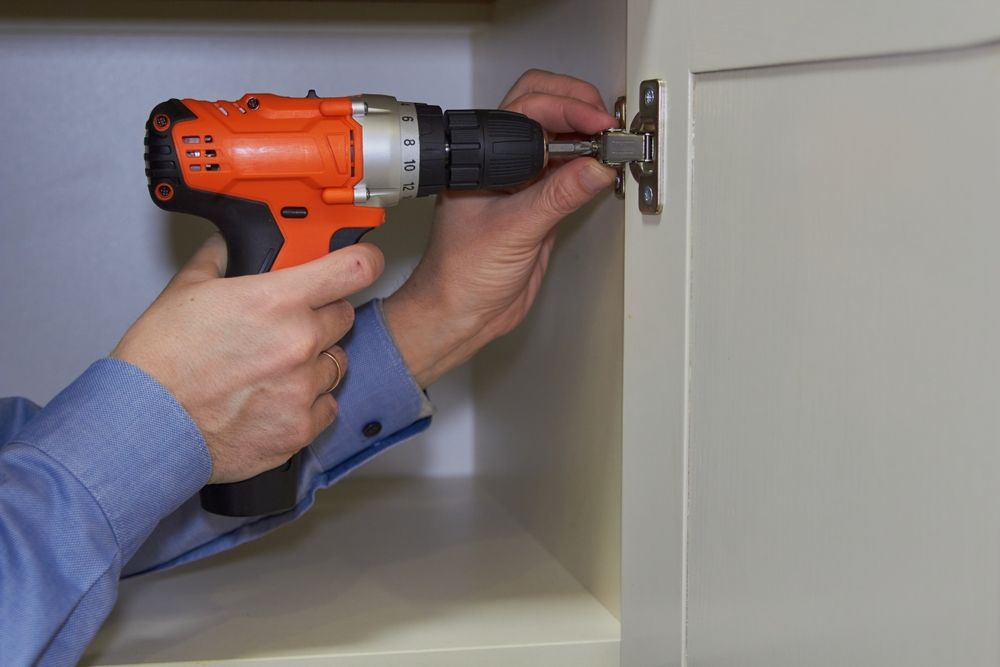 Una persona taladra un soporte en una pared blanca con un taladro inalámbrico naranja.