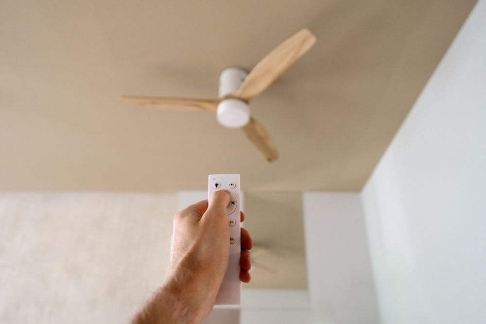 Una mano que sostiene un control remoto apunta a un ventilador de techo en una habitación.