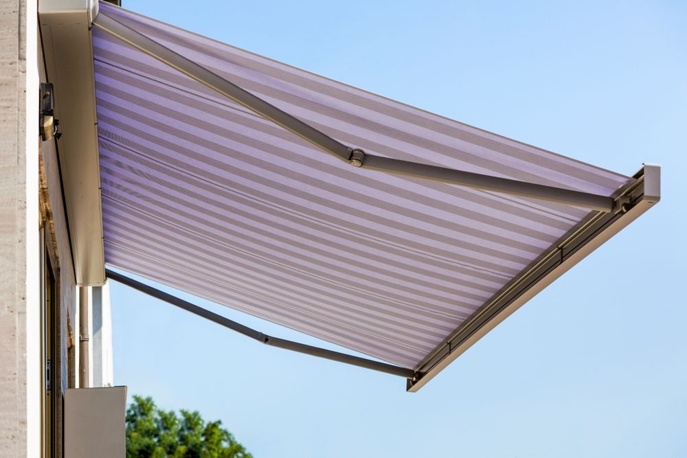 Un toldo retráctil a rayas se extendía desde un edificio contra un cielo azul.