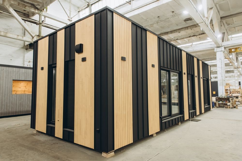 Edificio modular moderno con paneles verticales de color beige y negro dentro de un almacén.