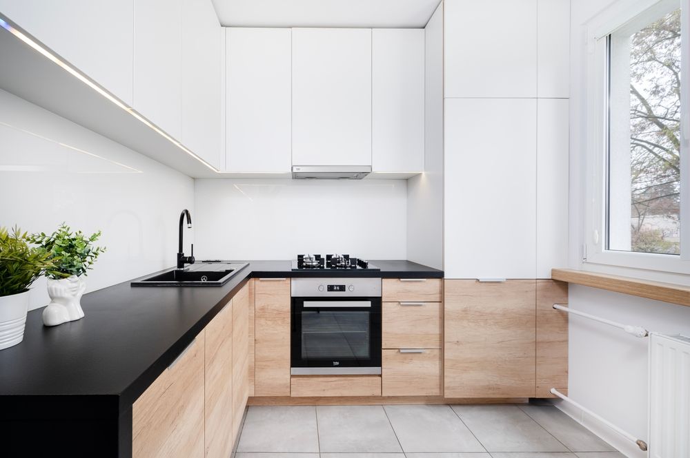 Cocina moderna blanca con encimeras negras, armarios de madera y una ventana con vistas a los árboles.