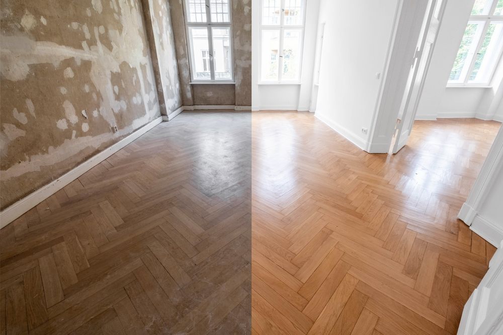 Habitación vacía con suelo de madera en espiga, paredes sin terminar y ventanas altas que dejan entrar la luz del día.