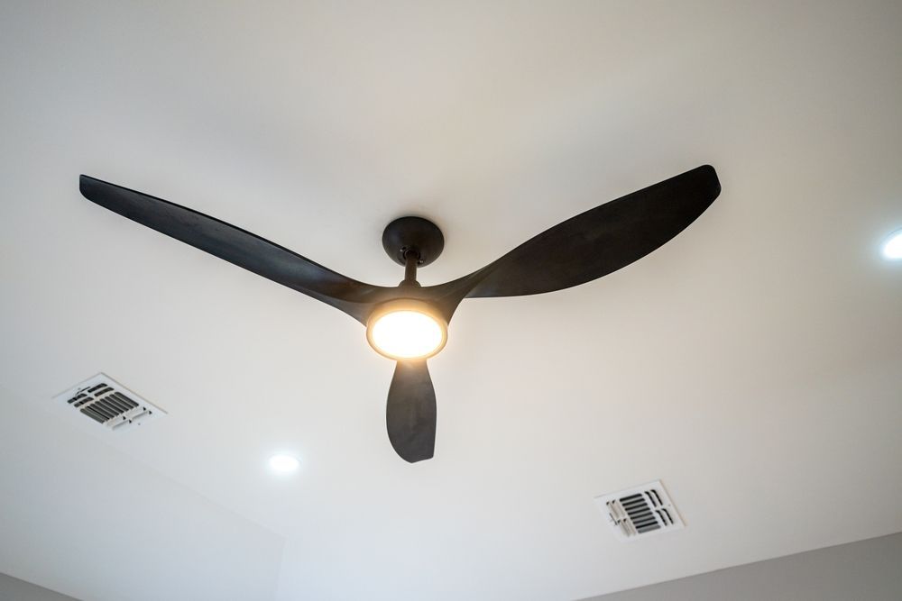 Ventilador de techo negro con luz sobre un techo blanco.