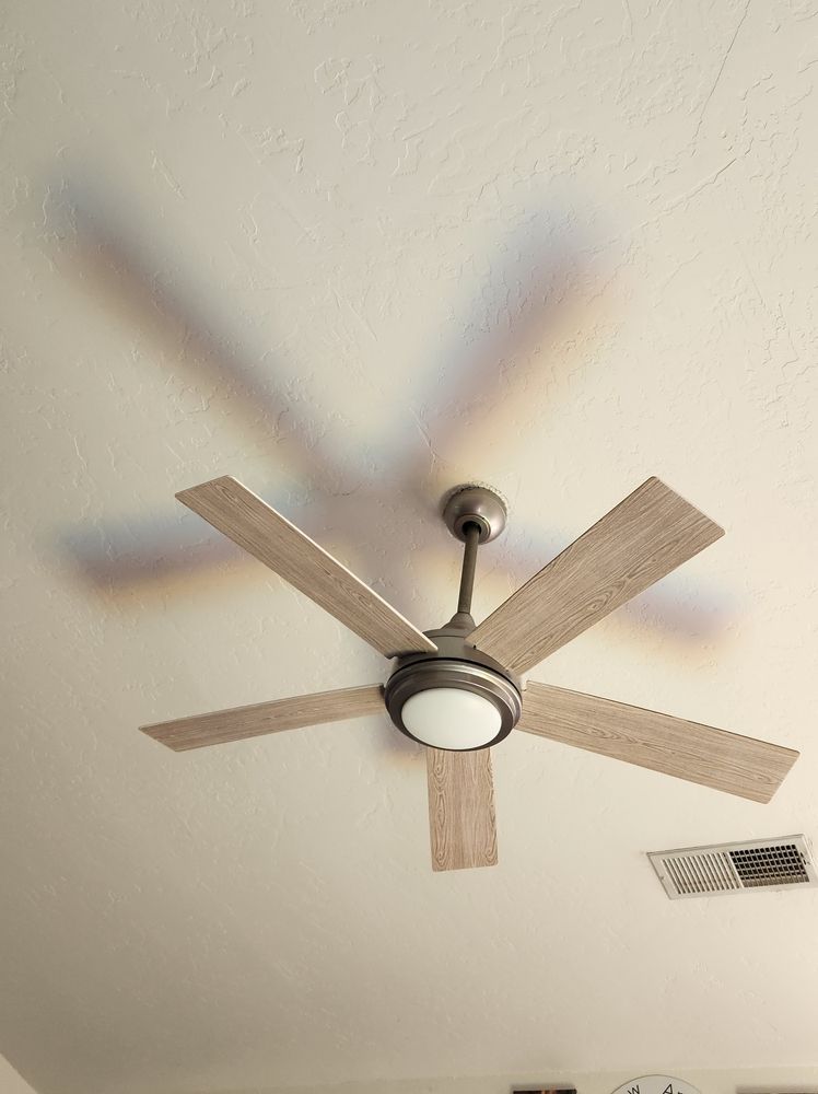 Ventilador de techo moderno con cinco aspas de madera y luces sobre un techo beige.