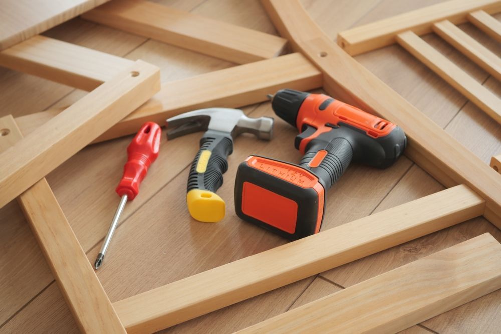 Caja de herramientas con destornillador rojo, martillo, alicates y taladro inalámbrico naranja sobre una superficie de madera.