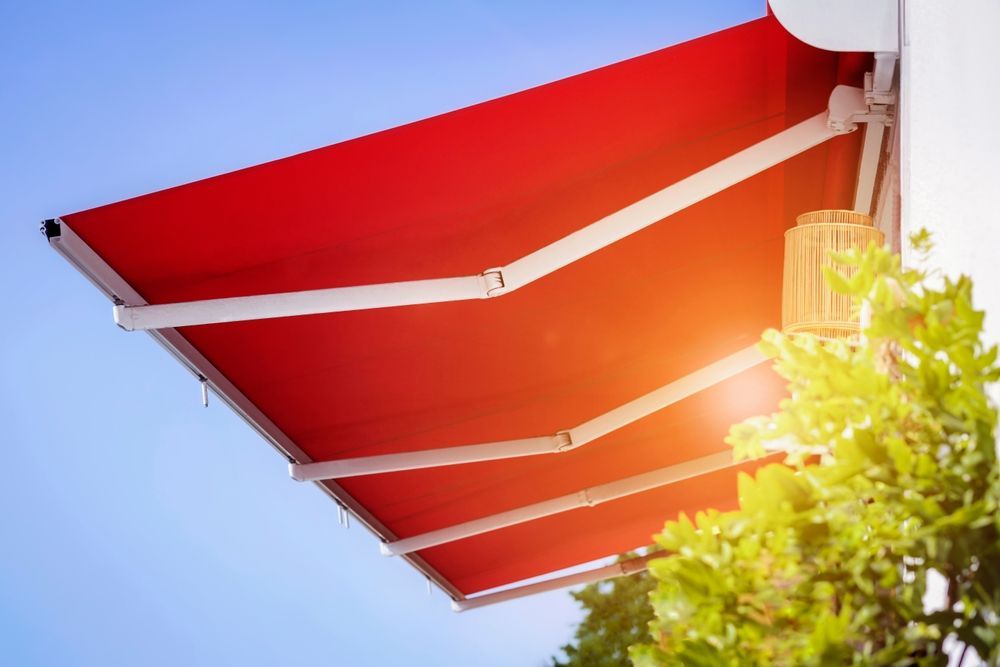 Toldo de rayas rojas y blancas contra un cielo azul con luz solar y hojas verdes en el borde.