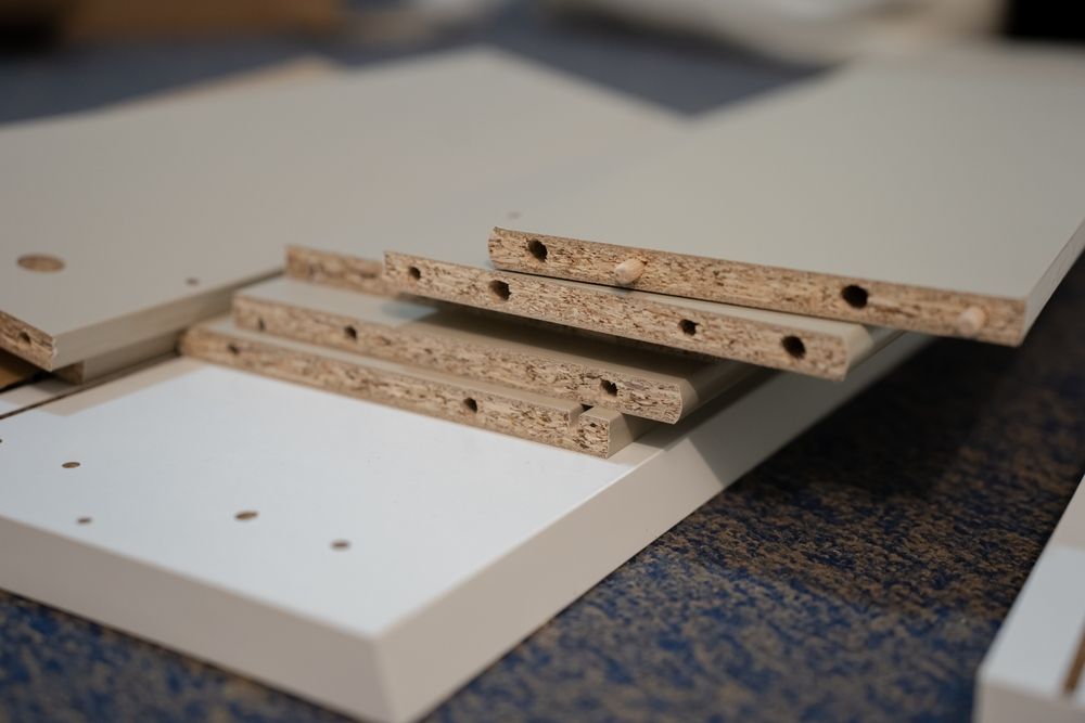 Tablones de aglomerado apilados sobre un panel blanco en un entorno que recuerda a un taller.