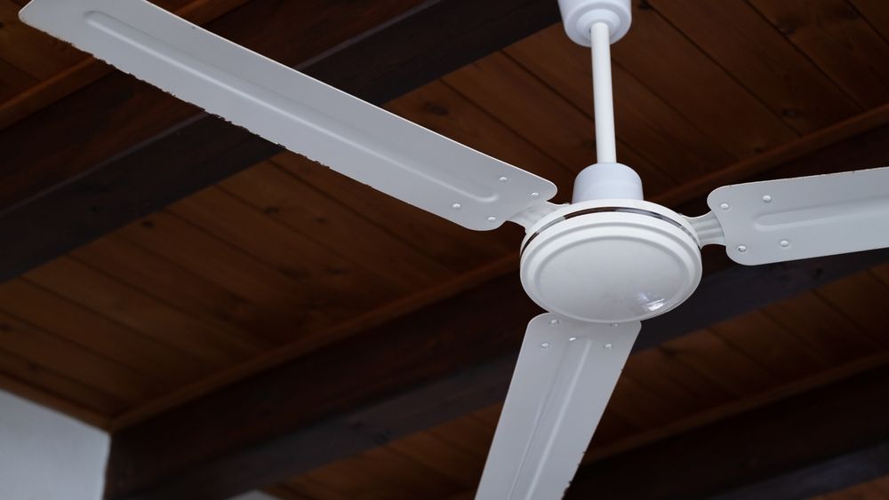 Ventilador de techo blanco de tres aspas sobre un techo de madera.
