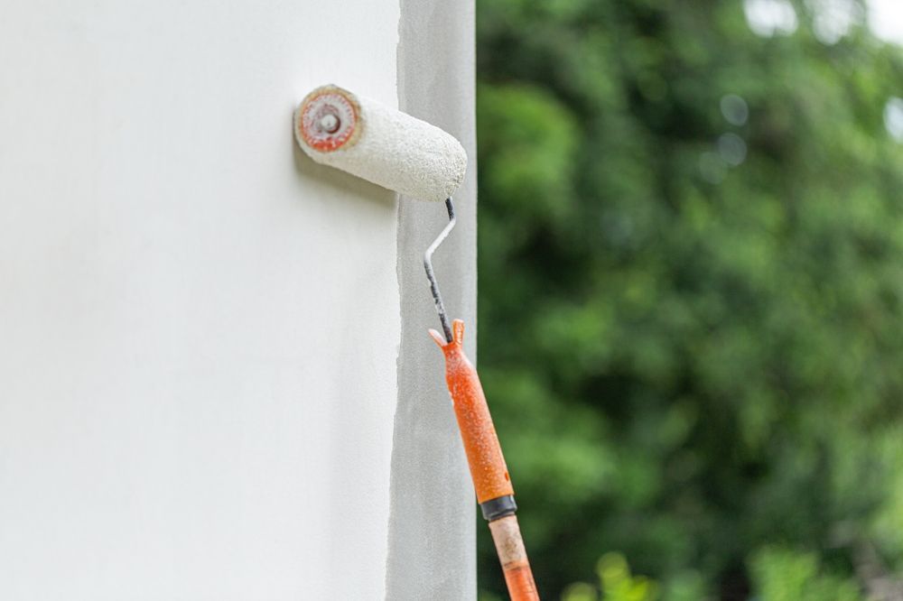 Rodillo de pintura aplicando pintura blanca a una pared exterior.