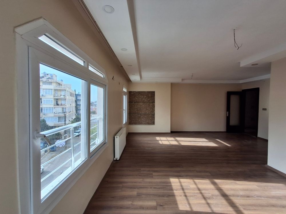 Sala de estar moderna y vacía con grandes ventanales, suelos de madera y luz natural en el suelo.