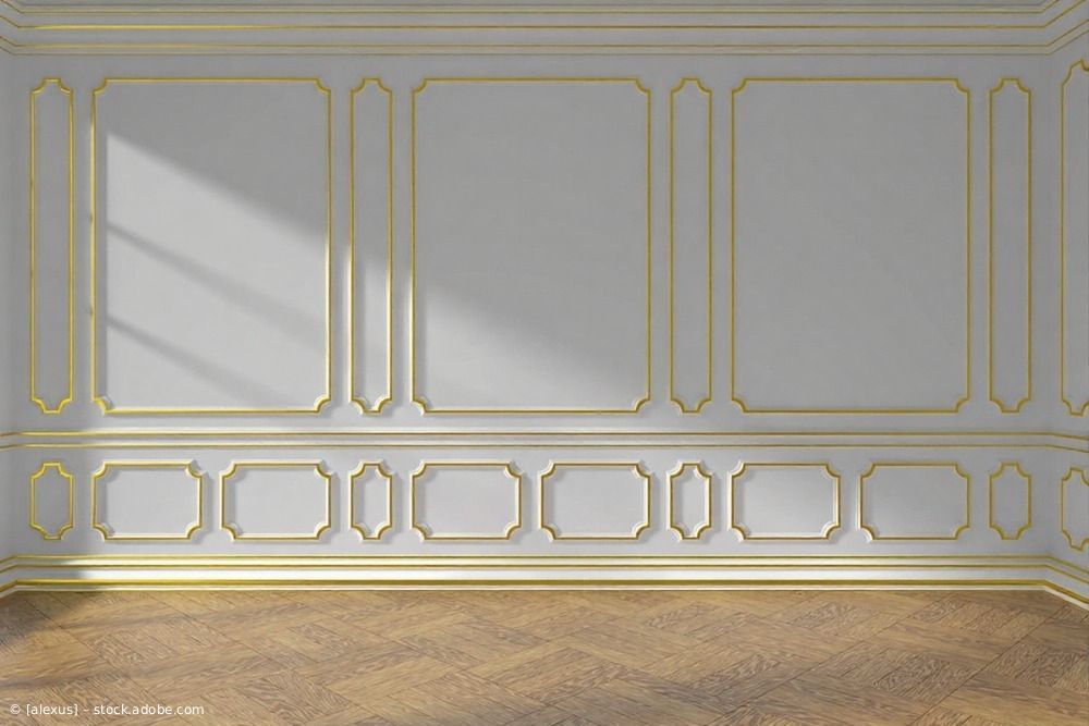Innenwand mit weißer Paneelverkleidung und goldenen Zierleisten, darüber ein Fischgrätenparkett aus Holz