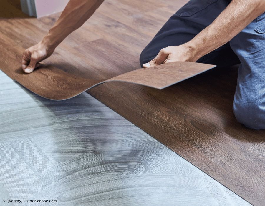 Eine Person kniet und verlegt vorsichtig Vinyl-Bodenplanken in Holzoptik auf einer Klebeschicht auf dem Unterboden.