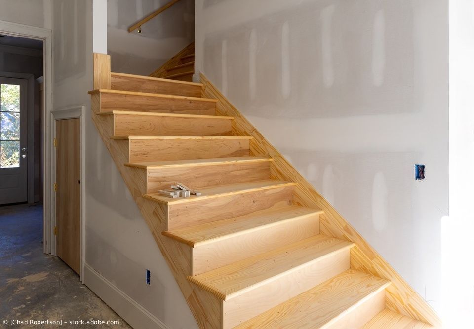 Eine im Bau befindliche Treppe mit Holzstufen und weißen Gipskartonwänden.