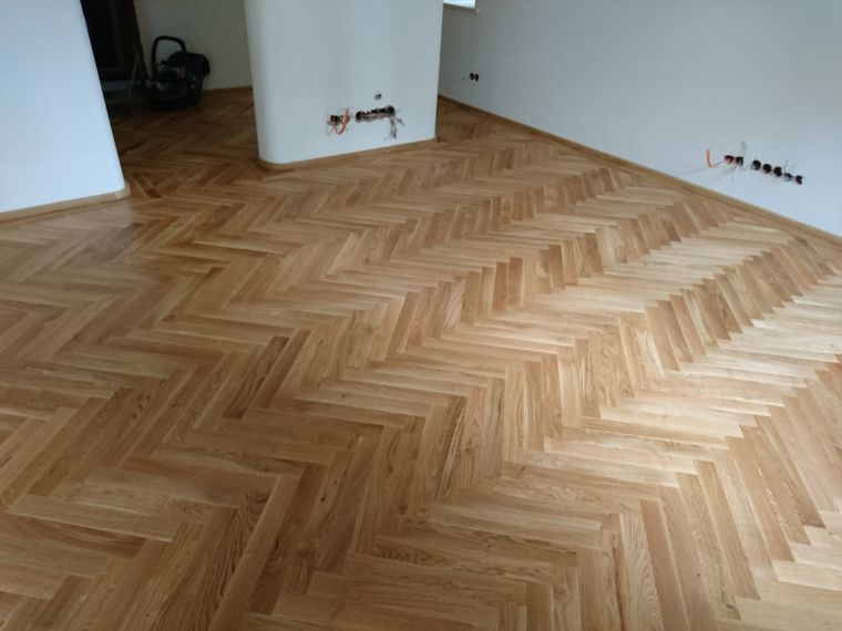 Ein neu verlegter, heller Hartholzboden mit traditionellem Fischgrätmuster in einem leeren Raum.