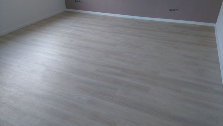 Ein leerer Raum mit hellem Holzboden und einer hellvioletten Wand mit weißen Zierleisten.