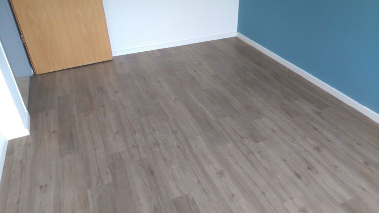 Ein leerer Raum mit hellgrauem Holzboden, weißen Wänden, einer blauen Akzentwand und einer Holztür.