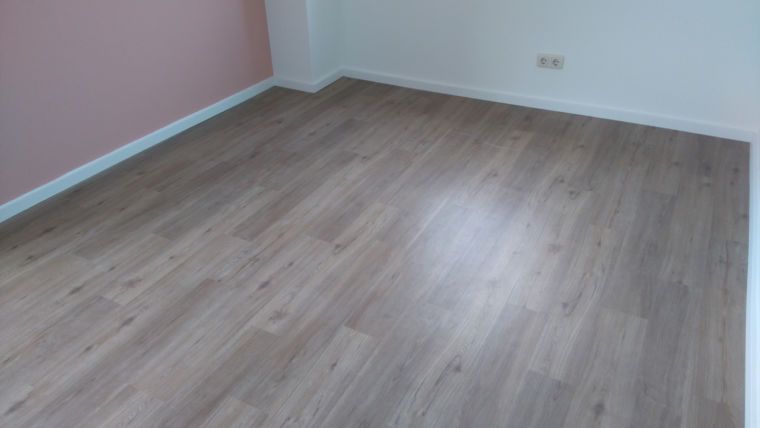 Ein leerer Raum mit hellem Holzboden, weißen Fußleisten und einer rosa Akzentwand.