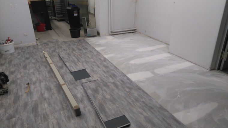 Ein Zimmer, in dem der Bodenbelag erneuert wird; die eine Hälfte des Bodens ist mit grauen Dielen in Holzoptik bedeckt, 